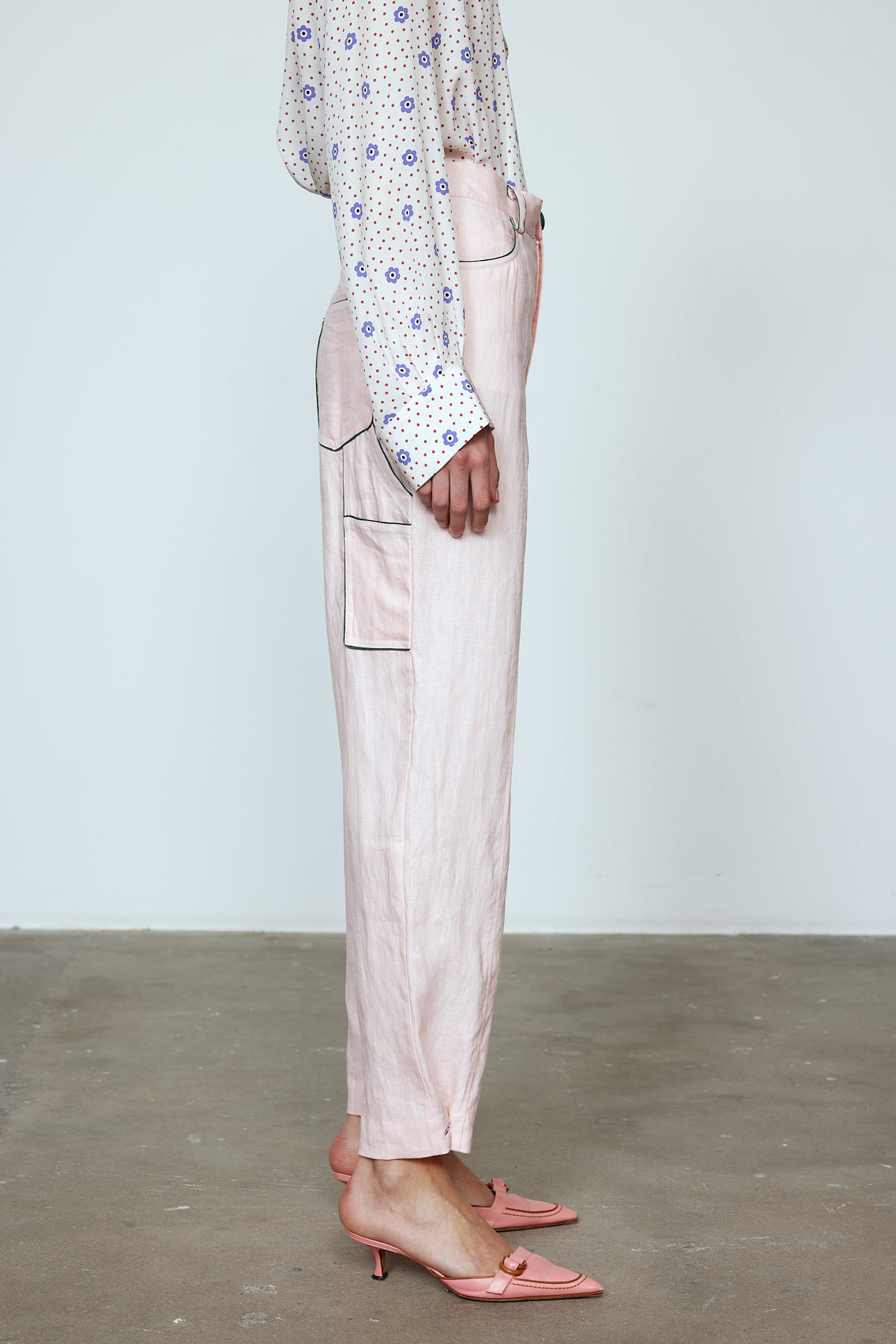 The Emma Pants in Baby Pink Linen. The pants feature cargo details on the side and large pockets with piping details in a contrasting color. Easily modify the shape of the pants with a button adjustment. Style them with a t-shirt, blouse, or a matching Emma Jacket in Baby Pink Linen. Also available in Orange and Navy.