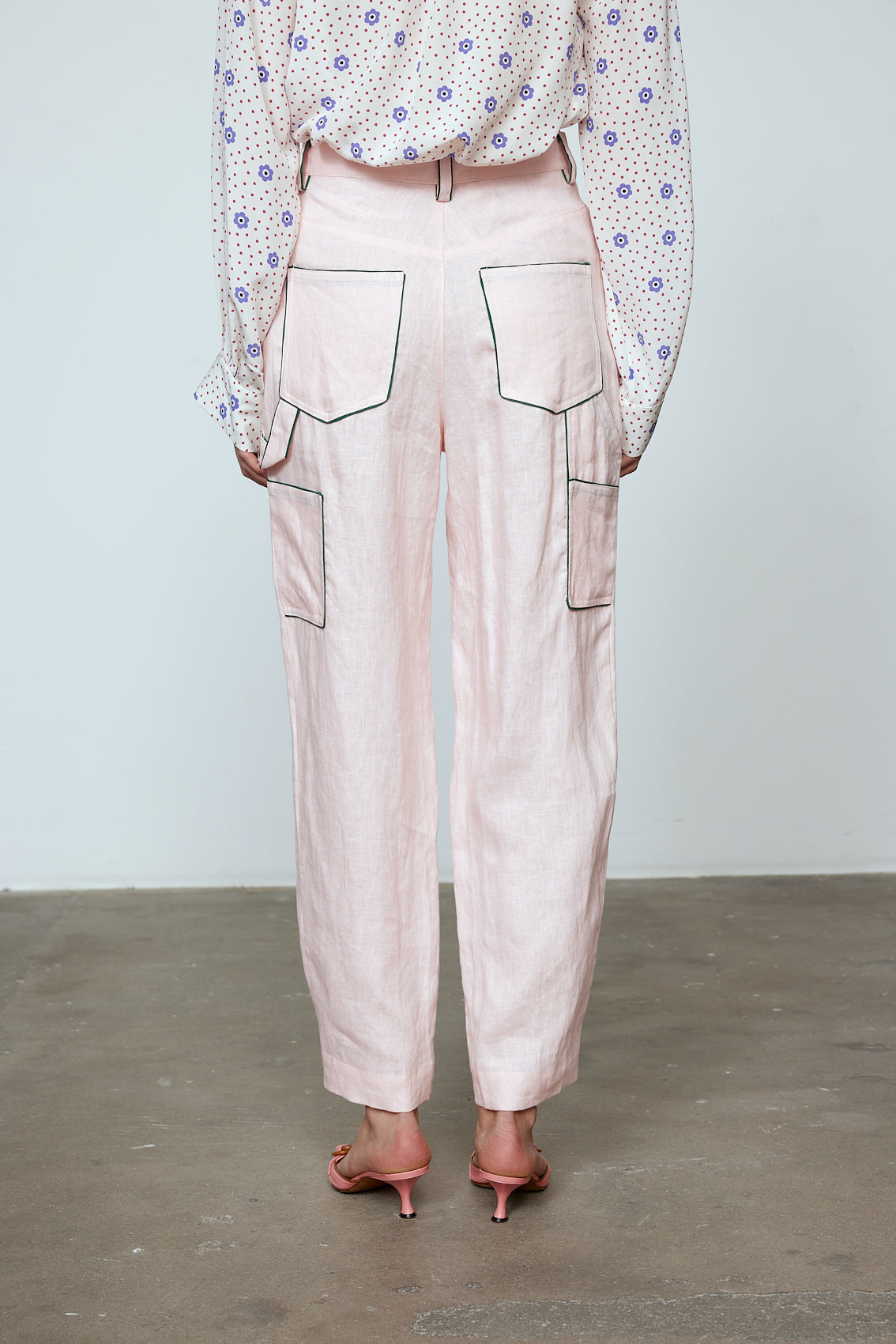 The Emma Pants in Baby Pink Linen. The pants feature cargo details on the side and large pockets with piping details in a contrasting color. Easily modify the shape of the pants with a button adjustment. Style them with a t-shirt, blouse, or a matching Emma Jacket in Baby Pink Linen. Also available in Orange and Navy.