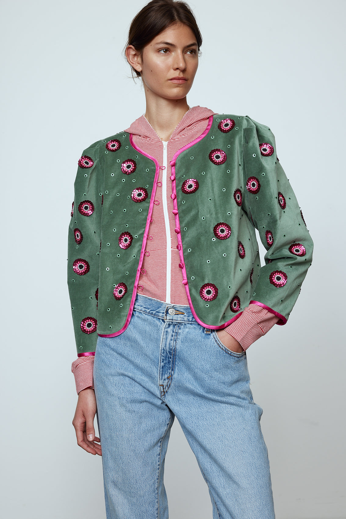 The Blanca Jacket in luxurious olive green silk velvet, exquisitely hand-embroidered by skilled artisans in our flower daisy pattern using beadings and sequins. The jacket features pink silk-button closings on the front and pink silk lining.