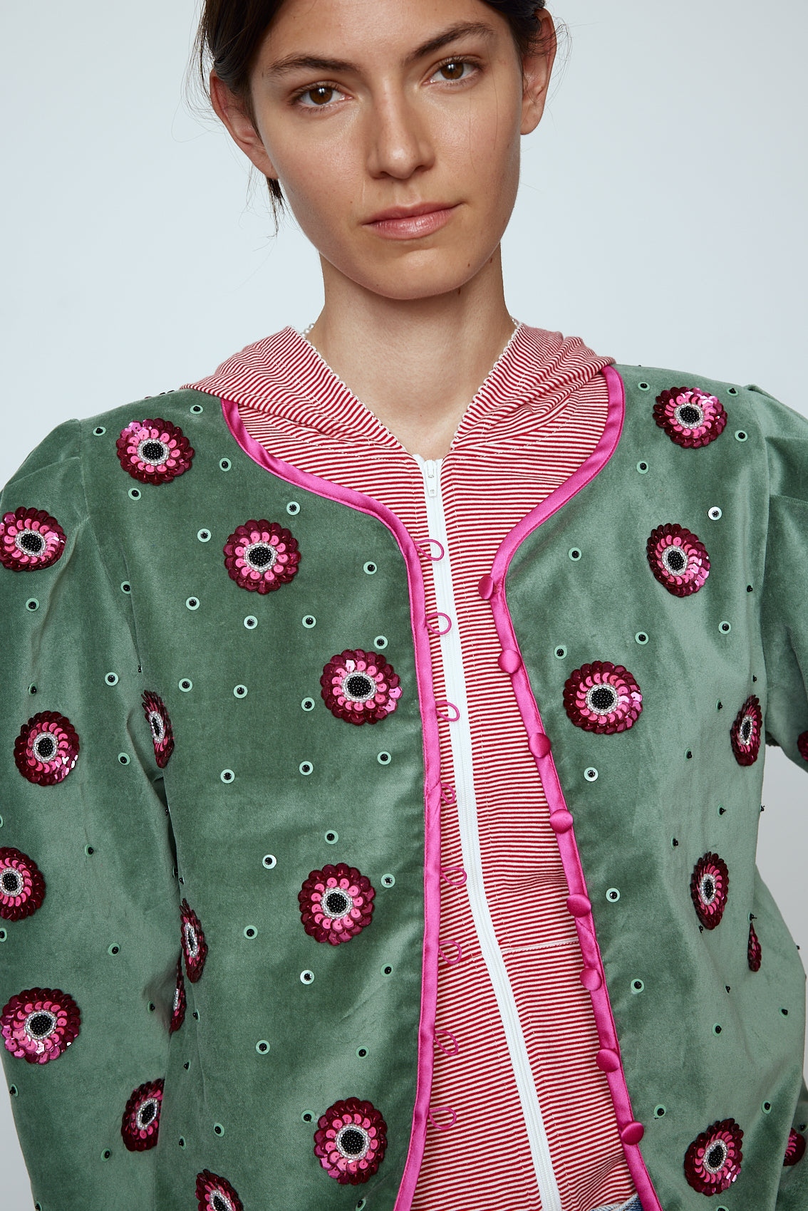 The Blanca Jacket in luxurious olive green silk velvet, exquisitely hand-embroidered by skilled artisans in our flower daisy pattern using beadings and sequins. The jacket features pink silk-button closings on the front and pink silk lining.