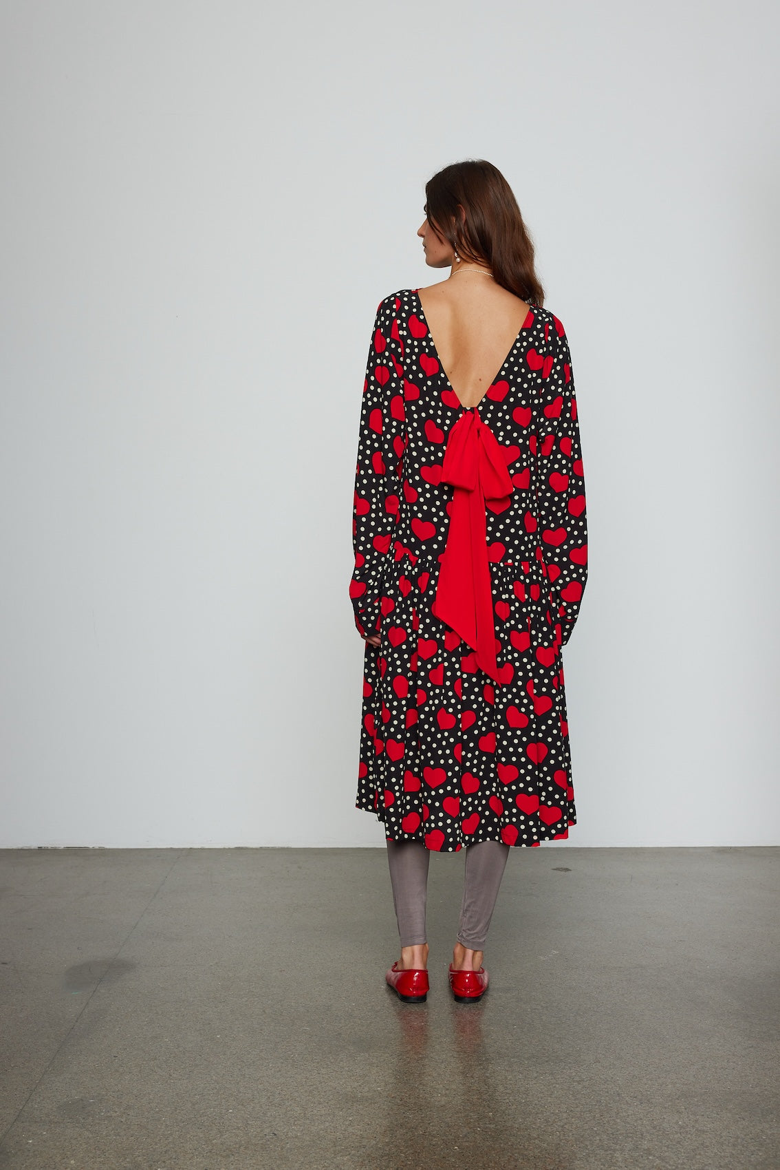 Caro Editions Holly Dress is an oversized style with a high neckline, low back with a large bow detail, and our long draped signature sleeves. The dress is made from soft silk crepe de chine featuring a heart print. Style it with an open shirt or denim jacket.