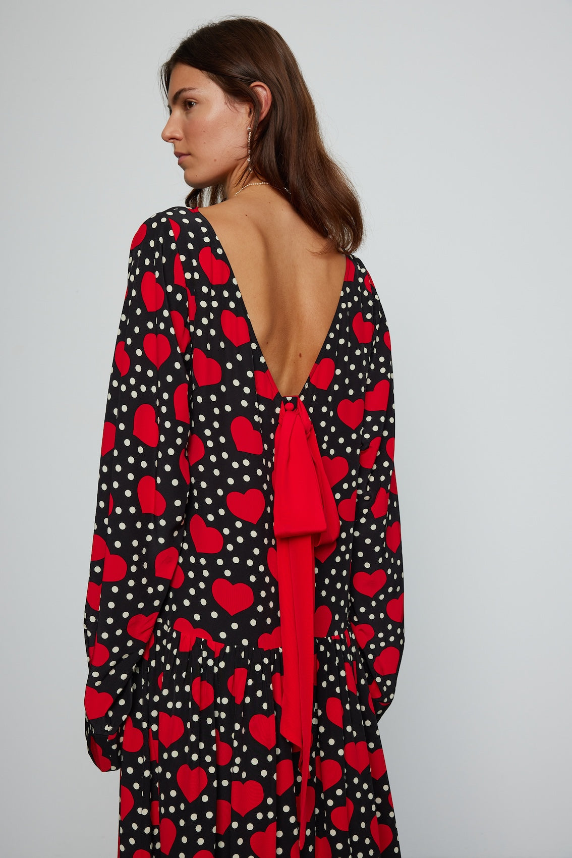 Caro Editions Holly Dress is an oversized style with a high neckline, low back with a large bow detail, and our long draped signature sleeves. The dress is made from soft silk crepe de chine featuring a heart print. Style it with an open shirt or denim jacket.