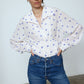 The Nikita Blouse in White Daisy Silk. This shirt features a fitted waist and signature Caro Editions sleeves with cuffs inspired by the party vibe of the 70s.  Style it on its own or with a top underneath.  Also available in Pale Pink Silk.