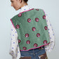 The Ravnbak Vest in Olive Green velvet with a pink lining. The vest is exquisitely hand-embroidered by skilled artisans in our flower daisy pattern using beadings and sequins. Style it over a shirt, dress, or top.  Also available in Baby Pink.