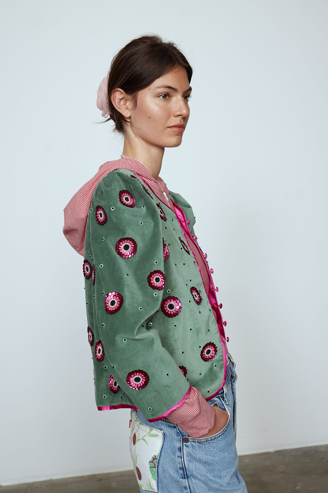 The Blanca Jacket in luxurious olive green silk velvet, exquisitely hand-embroidered by skilled artisans in our flower daisy pattern using beadings and sequins. The jacket features pink silk-button closings on the front and pink silk lining.