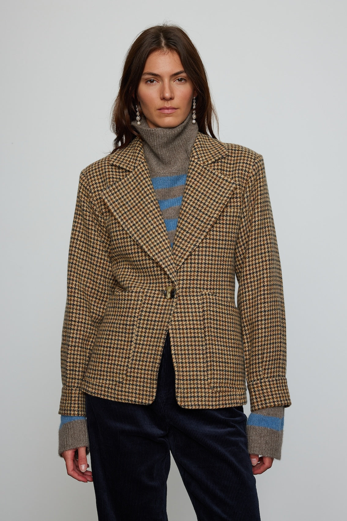 Caro Editions The Annika Jacket in a classic houndstooth tweed The jacket features a single-button closing at the front, wide padded shoulders, and large front pockets. The jacket is slightly fitted around the waist.  Material: 100% wool. Lining: 100% viscose.
