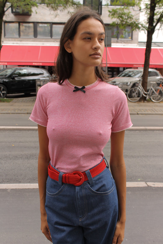 Caro Editions' new signature line in jersey cotton.  The Caro T-shirt is a fitted style with short sleeves, a ribbon bow detail at the front, and embroidered Caro Editions logo on the back.   Also available in White and Black White stripe.  Style the Caro T-shirt under shirts or dresses, or wear them on their own.  Material: 95% cotton, 5% elastane. Bow: 100% Polyester.  The model is 175cm (5'9") and is wearing a size S.